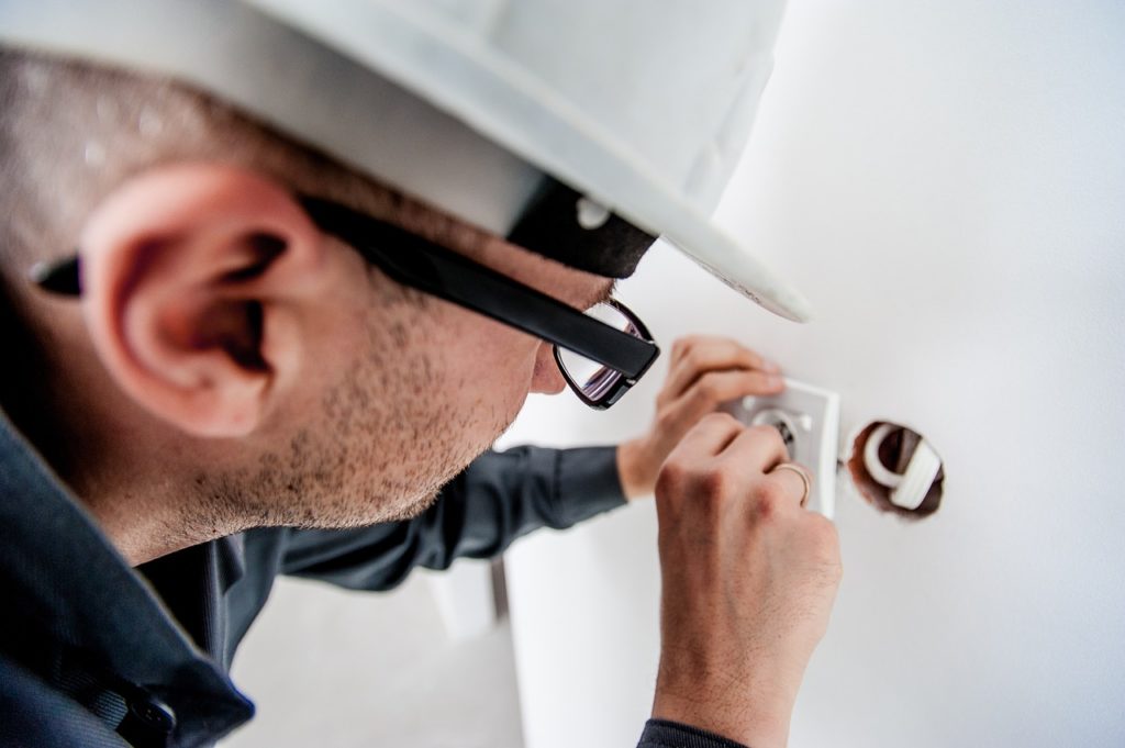 Image of an electrician with a hard hat working on an outlet.
