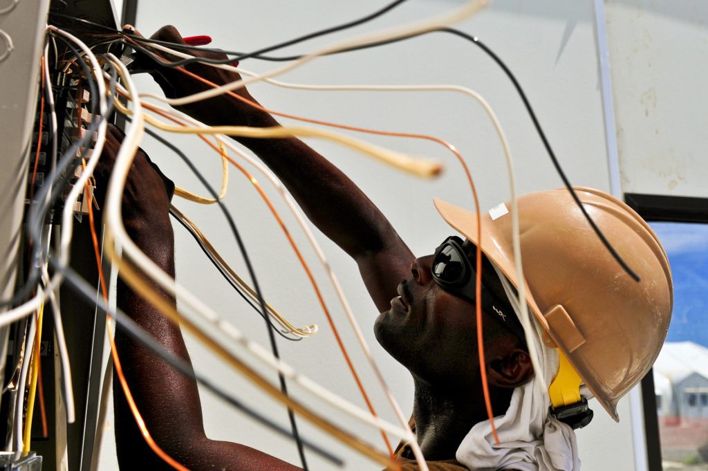 An electrician wearing a hardhat works with an array of insulated multicolored wires