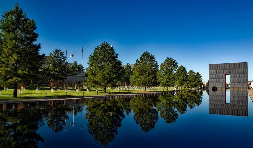 Oklahoma City Memorial reflected in water, at the end of a row of trees.