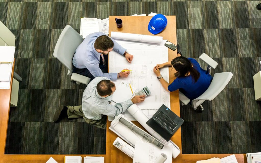 Three people sit around a table and assess the logistics of an upcoming construction project.