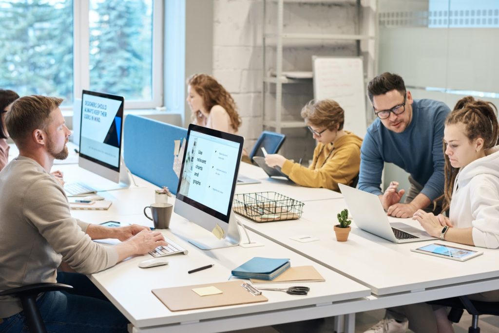 A team of people working on desktop computers all seated around a large group table.