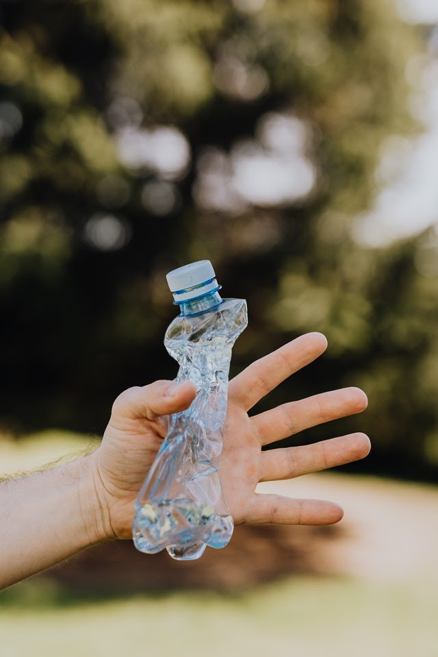 A hand holding an empty, crushed plastic water bottle.