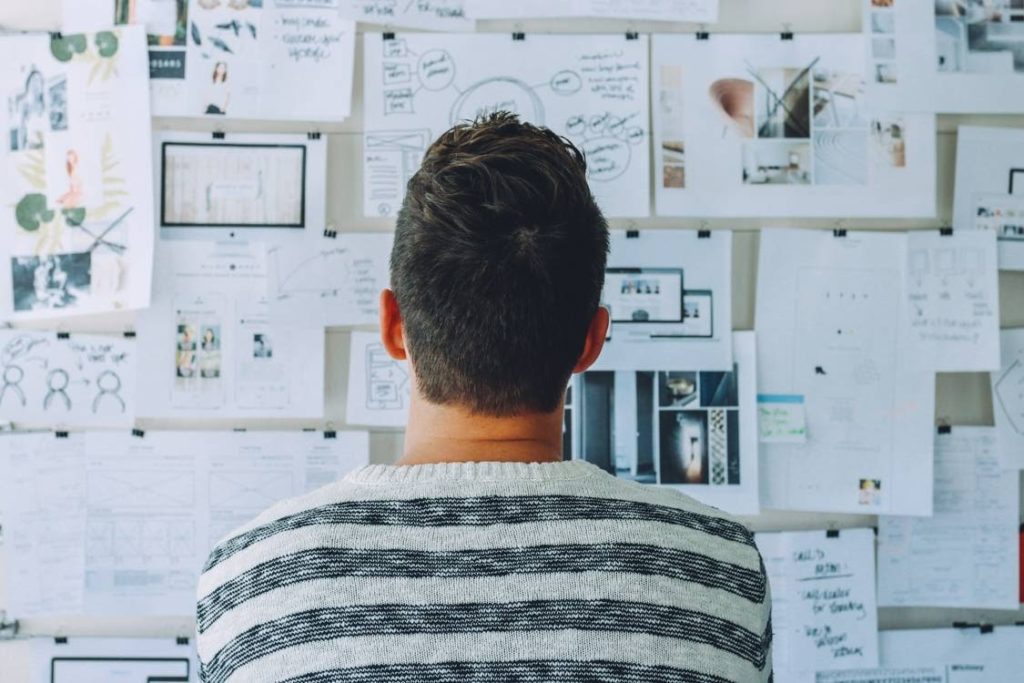 A person staring at various graphs, images, and other paper documents clipped to the wall.