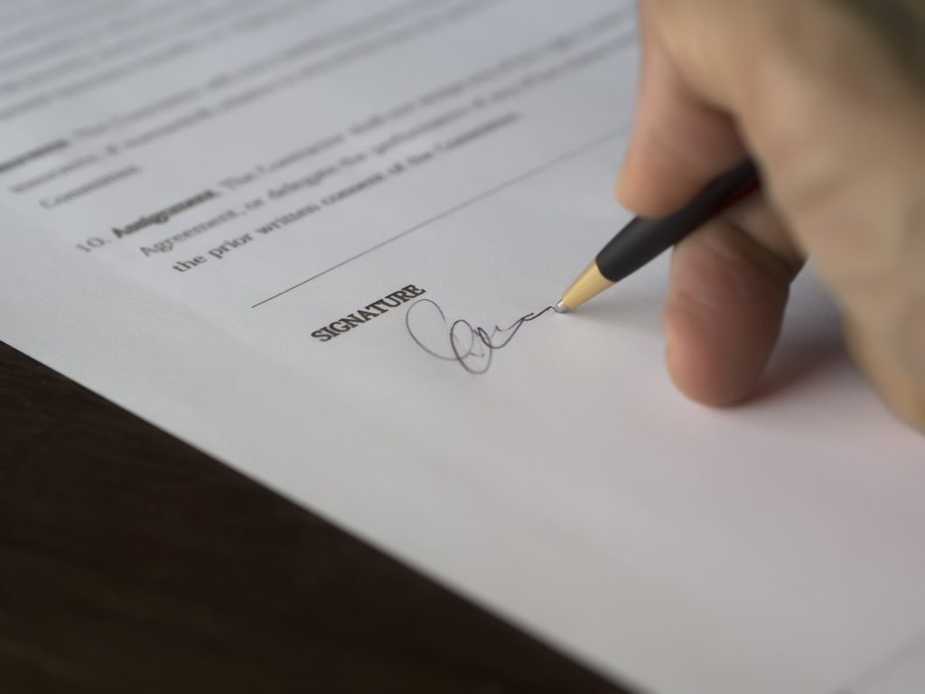 Close-up of a person’s hand as they apply their signature to a business license.