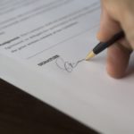 Close-up of a person’s hand as they apply their signature to a business license.