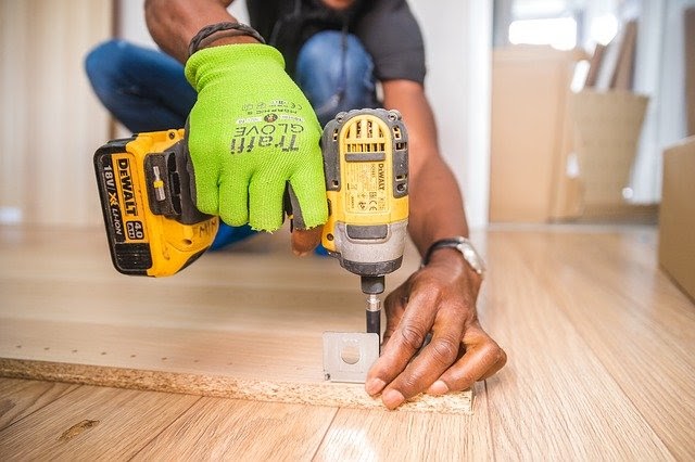 Handyman using yellow drill bracket on shelf on hardwood floor.