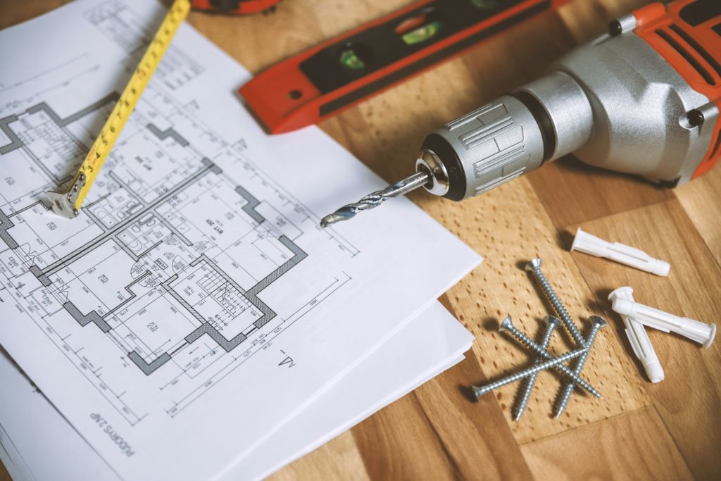 Floor plans, a level, power drill, and screws on a table.