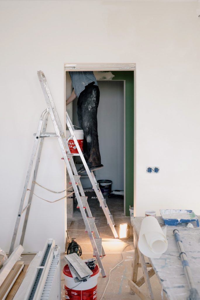 Two ladders in a room with an individual on one of them painting. 