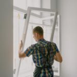 Handyman holding windo pane up in window frame to re-install it