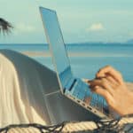 Close up of female hands working on laptop lying in hammock at sand beach of tropical island. Freelance outdoor work concept
